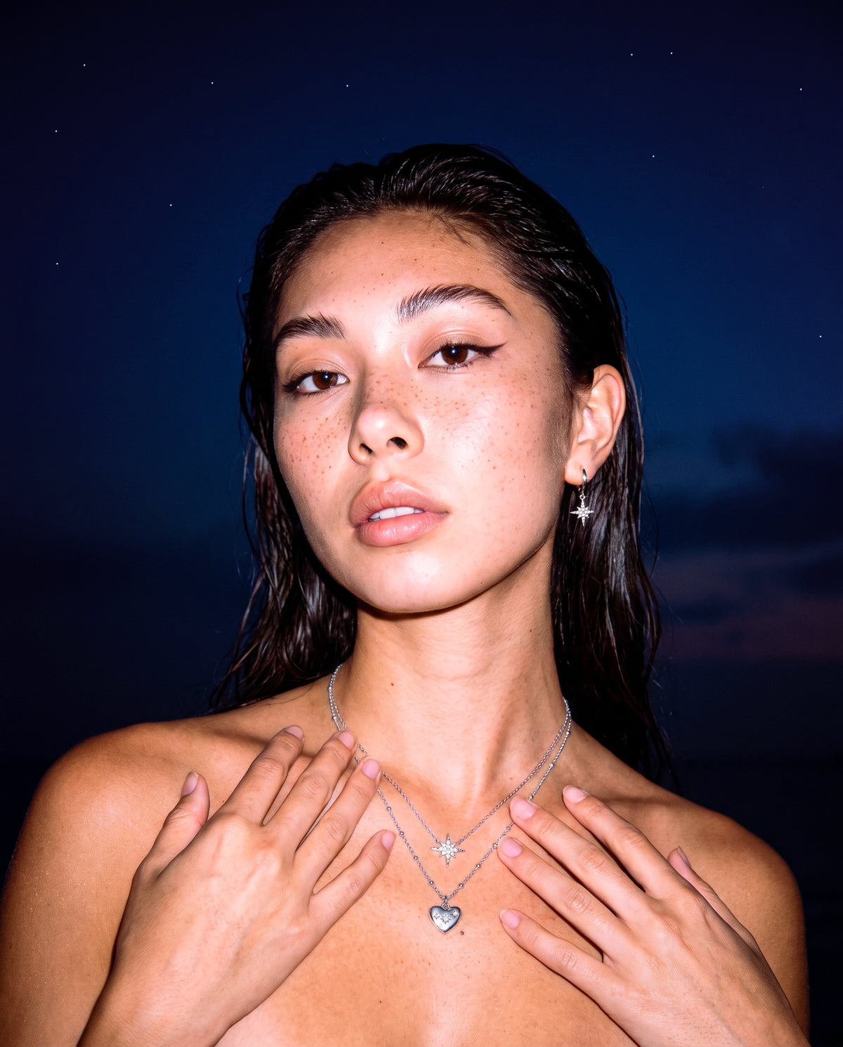 Silver celestial star and heart necklaces worn under a night sky