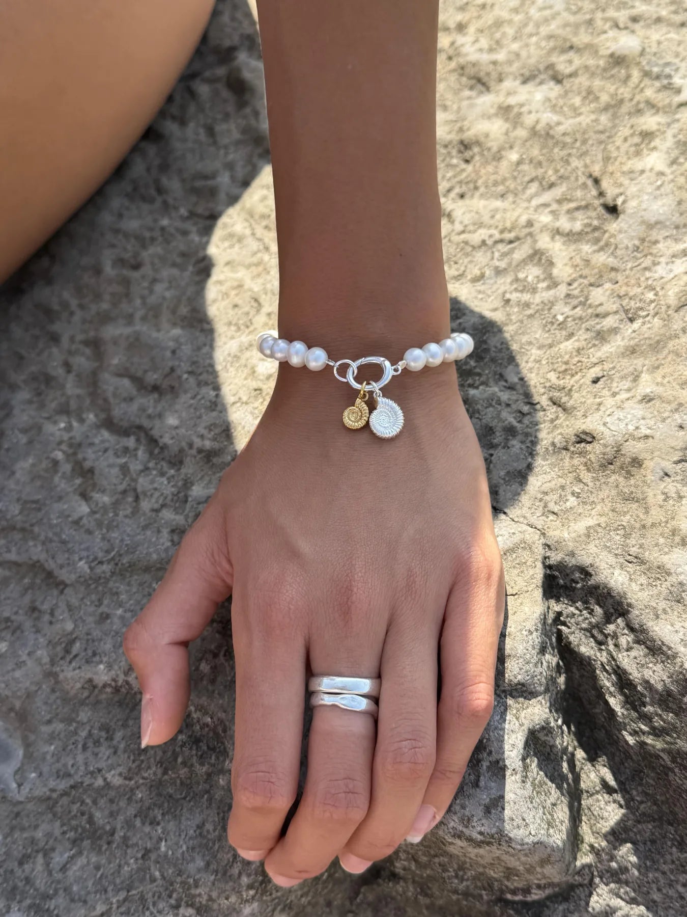 Pearl charm bracelet with ammonite charms worn on the wrist