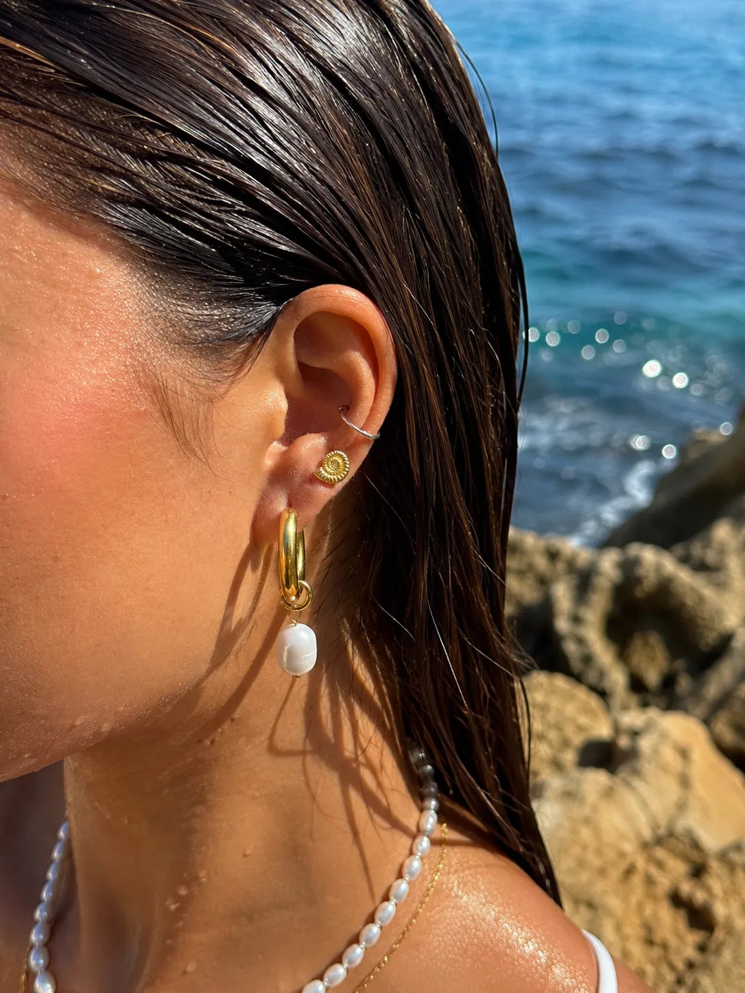 Gold pearl hoop earrings and ammonite stud styled by the sea