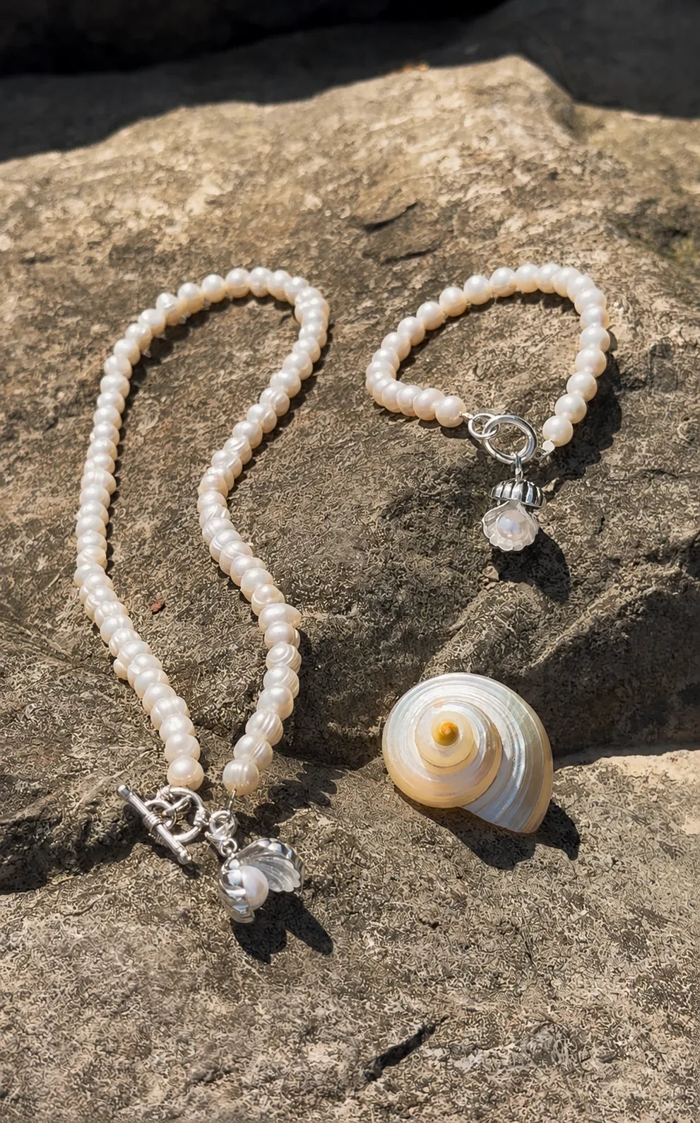 White pearl necklace and bracelet with shell charm on coastal rocks