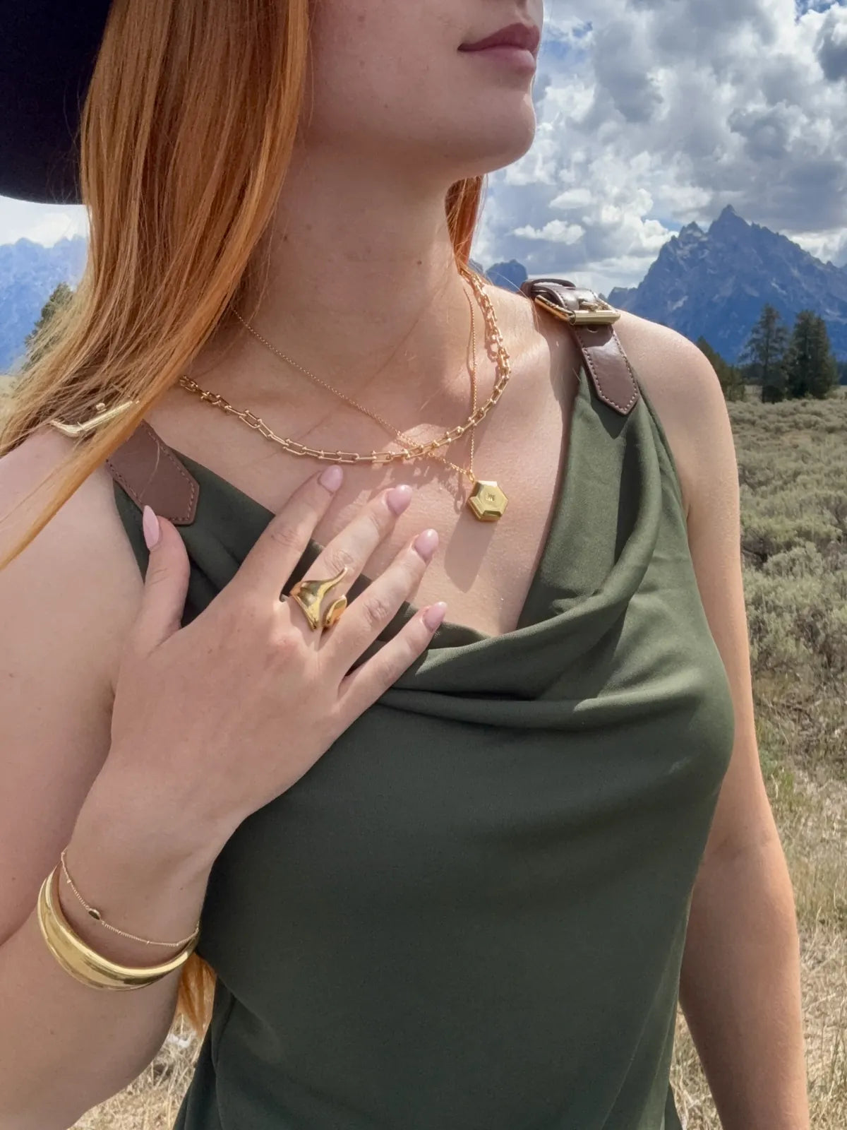 Gold hexagon locket, ball link necklace, bone cuff bangle and molten gold ring worn against Wyoming mountains