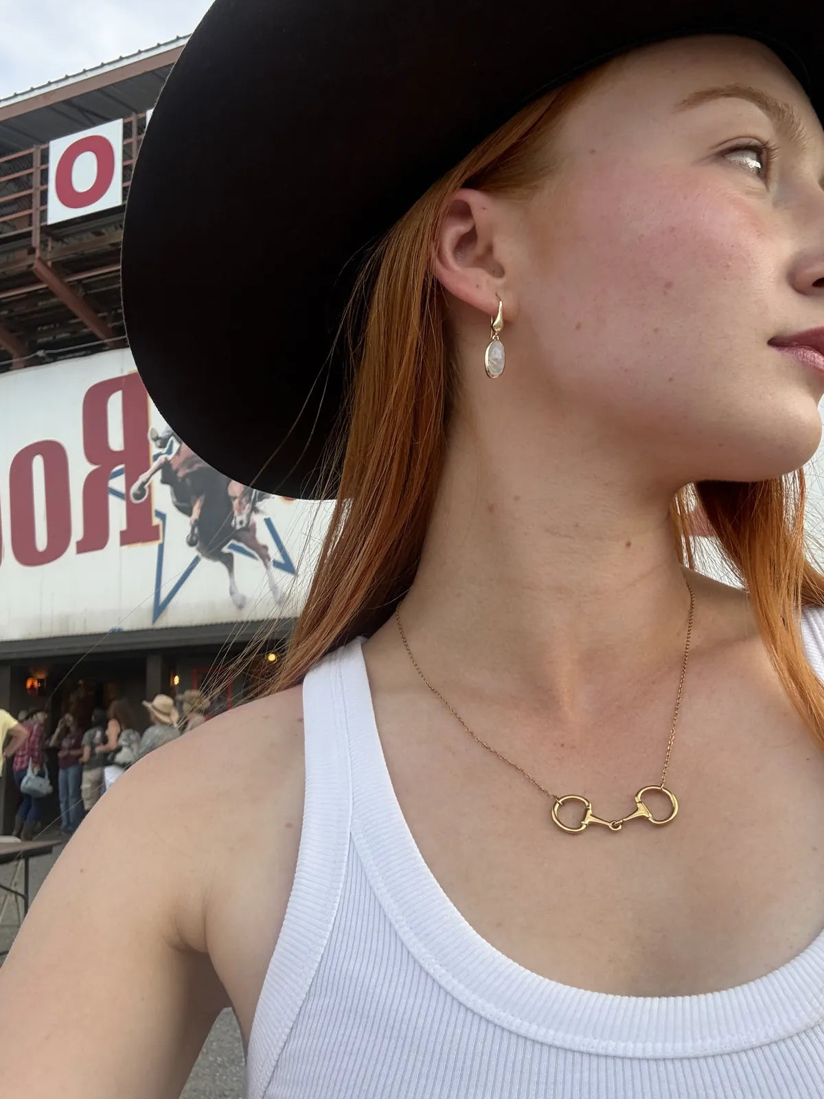 Moonstone drop earrings and snaffle gold necklace worn with a cowboy hat at the rodeo